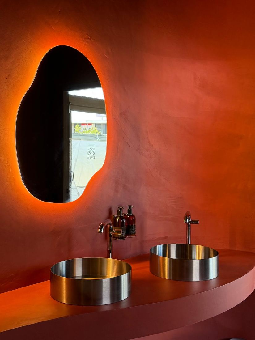 Miroir organique rétroéclairé sur mur terracotta, vasques inox — Studio Clo